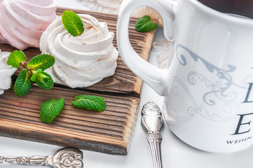 White creamy marshmallow handmade. Adorned with mint leaves. Tea in a white cup with a blue ornament. On a wooden background. Close-up.