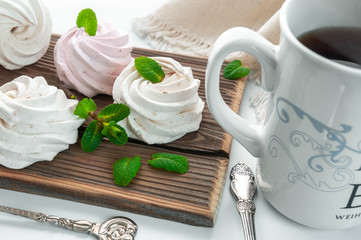 Handmade cream and strawberry marshmallows. Adorned with mint leaves. Tea in a white cup with a blue ornament. On a wooden background. Close-up.