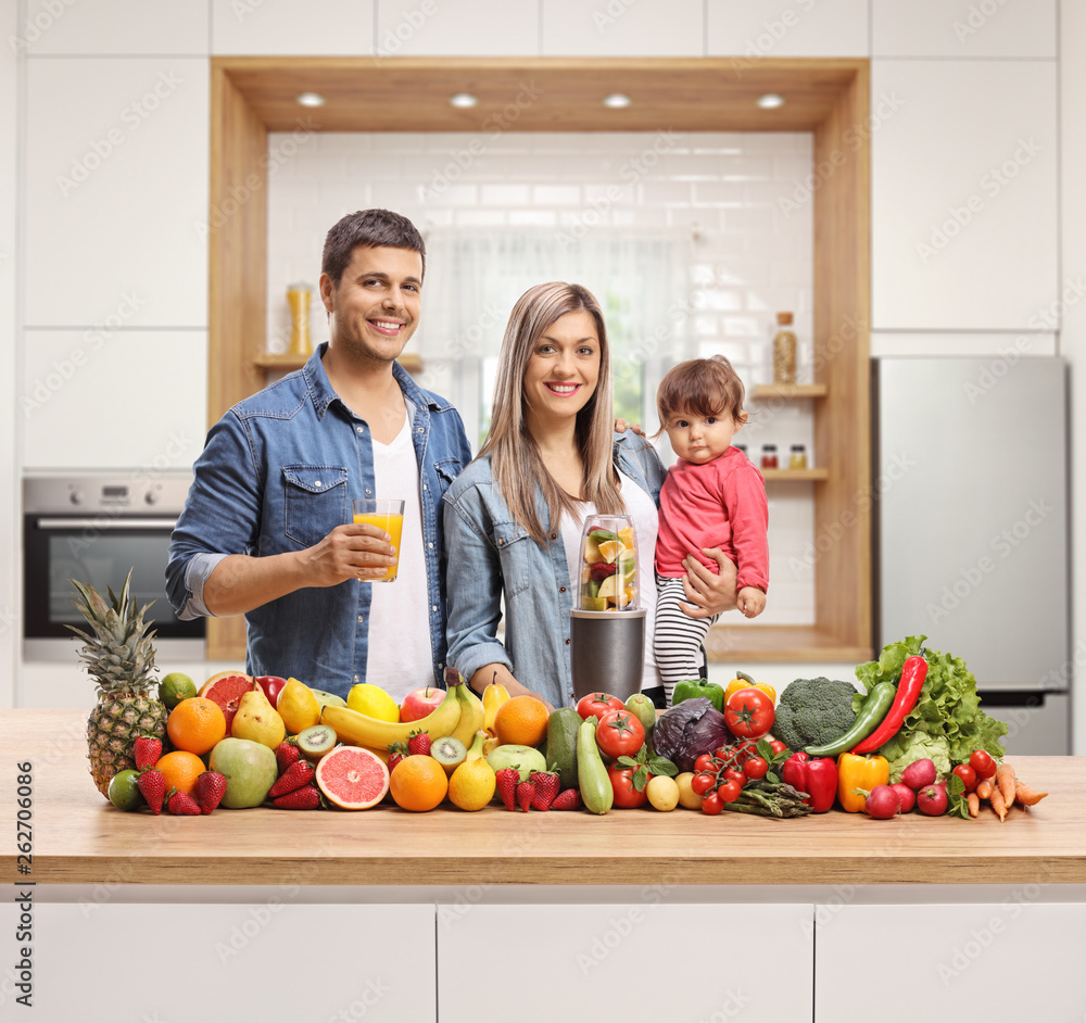 Wall mural family with a baby in a kitchen with fruits and vegetables and a blender