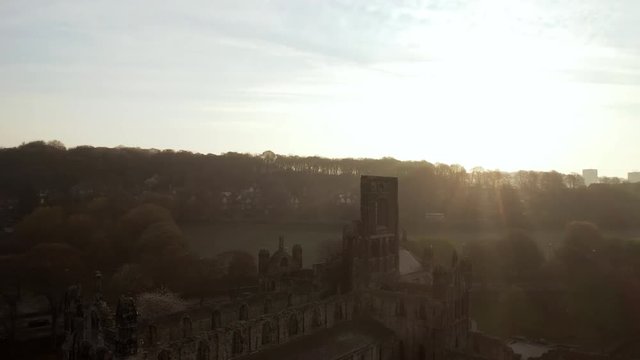 Aerial Tracking Shot of Kirkstall Abbey at Dawn with Lens Flare on Sunny Spring Day facing Sun