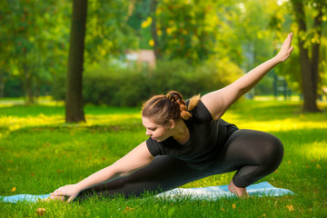 flexible woman plus size in the park on the lawn performs stretching exercises