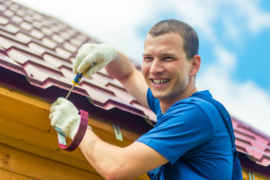 Happy Man Is Repairing The Roof Of The House, A Portrait On The Background Of Tiles