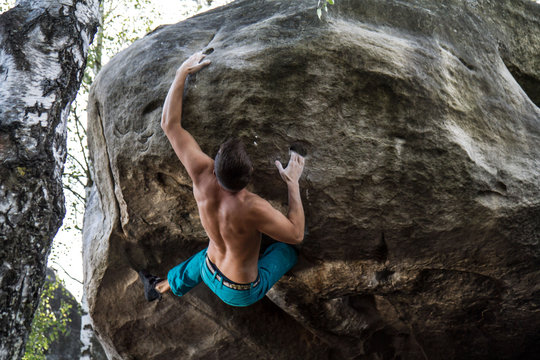Jeune homme avec le dos muscl&eacute; qui escalade un rocher en for&ecirc;t torse-nu, d&eacute;termin&eacute;, en pleine effort de grimpe intense