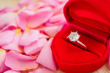 elegant wedding diamond ring in red heart jewelry box on beautiful pink rose petal background close up