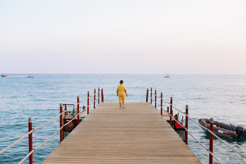 Boy walking on the pier and looking at the sea horizon and blue sky. Vacation at sea. Summer time sea vacation background 