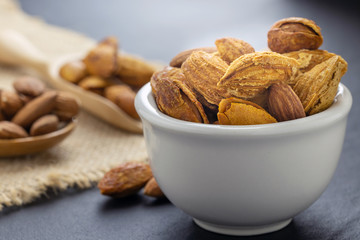 Almonds in a black bowl against dark rustic wooden background