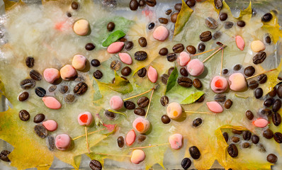 Background of  black coffee beans, red small apple, berry of goji and yellow leaves of maple   frozen in ice