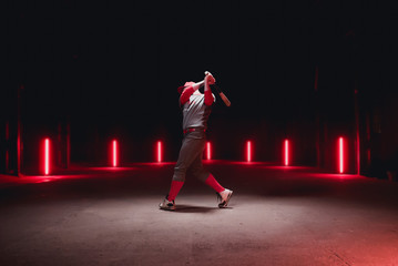 Caucasian professional baseball player batter posing against dark background in a large abandoned...