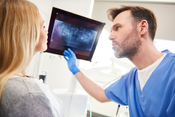 Naklejka na ściany i meble Dentist pointing at x-ray and examining patient the woman's teeth