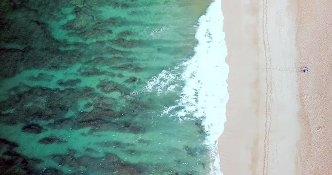Aerial: Turquoise Ocean, Gentle Waves & Sandy Beach with People from a Distance in Oahu, Hawaii