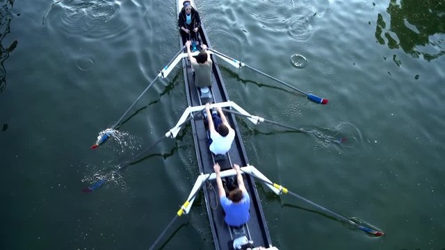 Rowers training on a competition rowing boat in a water canal. View from above.