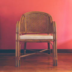 Wicker chair on the wooden floor, red wall background. Furniture, relax, vintage concept. Close-up, front view, copy space, square format, toned