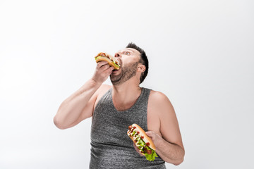 hungry overweight man in tank top eating hot dog on white