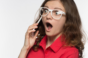 Beautiful girl in glasses in surprise opened her mouth talking on the phone on a white background