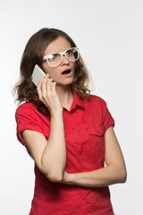 Naklejka premium Beautiful girl in glasses in surprise opened her mouth talking on the phone on a white background