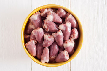 Raw chicken hearts in a yellow bowl on a white wooden table. Top view.