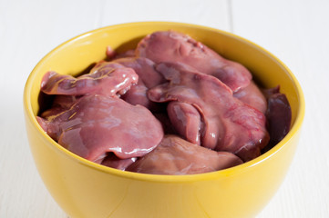 Raw chicken livers in a yellow bowl on a white wooden table. Close-up.