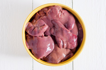 Raw chicken liver in a yellow bowl on a white wooden table. Top view.