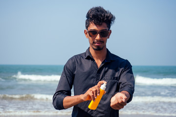 happy young african man on the beach.India model male holding a bottle of sunscreen student...