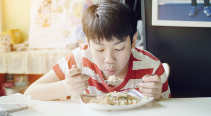 Cute Thai boy eating fried rice food on the white table in the living room.