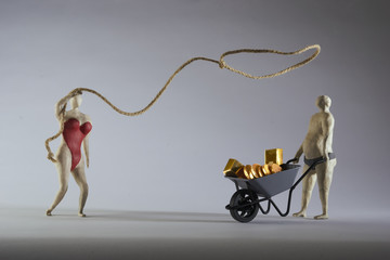 Sexy woman throws a lasso on a rich man.Wheelbarrow filled with gold.  Isolated on grey background. Studio Shot. With space copy text. - obrazy, fototapety, plakaty