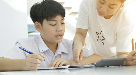 Asian mother helping her son doing homework on white table.