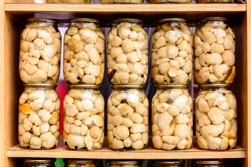 Delicious delicious white marinated mushrooms in glass jars on shelves.