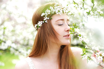 Beautiful redhead girl surrounded by blooming trees. Spring season is magic.