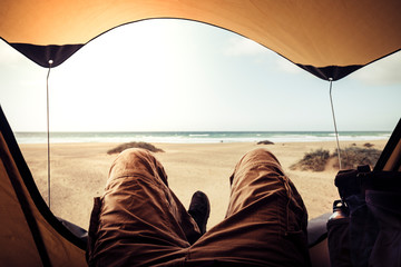 Alternative vacation concept with man in trekking clothes laying outside the tent campiing free at the beach looking the ocean horizon and enjoying the freedom - outdoor natural tourism for traveler