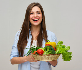 smiling woman in blue shirt holding big plate with fresh vegetables.