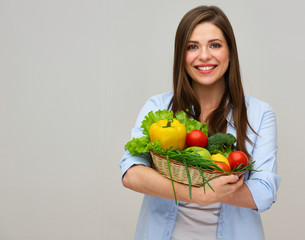 smiling woman in blue shirt holding big plate with fresh vegetables.