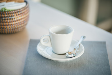 Coffee small cup with saucer, coffee spoon and napkin on a wooden table