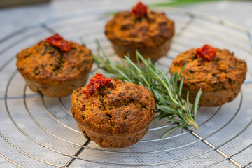 4 homemade hearty muffins with fresh herbs and dried tomatoes lying on a cake grid with a rosemary twig