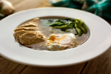 Homemade soup with poached egg, boiled chicken and spinach. On wooden table. Ginger. Garlic. Ingredients. Homemade.