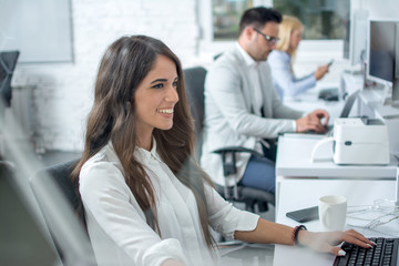 Beautiful smiling young woman working on computer at her workplace in office