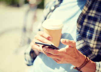 leisure, technology, communication and people concept - close up of man with smartphone and coffee cup texting message on city street