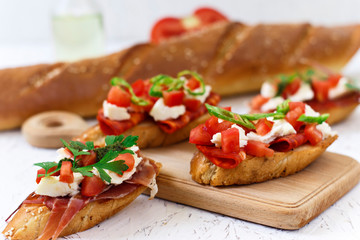 Italian appetizer - bruschetta with tomatoes, chili, sausage and cheese on a wooden board