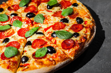Pepperoni Pizza with Mozzarella cheese, salami, olive, pepper, Spices and Fresh spinach. Italian pizza on Dark grey black slate background