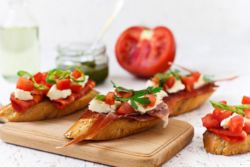 Italian appetizer - bruschetta with tomatoes, chili, sausage and cheese on a wooden board
