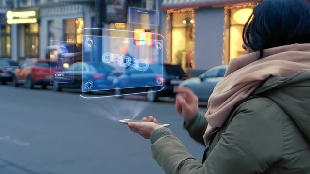 Unrecognizable woman standing on the street interacts HUD hologram with chain. Girl in warm clothes with a scarf uses technology of the future mobile screen on background of night city