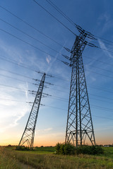 Riesiger Hochspannungs &ndash; Strommast auf einem Feld bei Sonnenuntergang, Hochformat