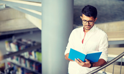 education, high school, university, learning and people concept - hindu student boy or young man reading book on stairs at library