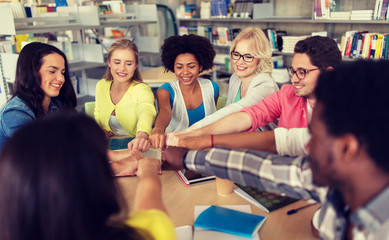 education, school, teamwork and people concept - group of international students sitting at table and making fist bump