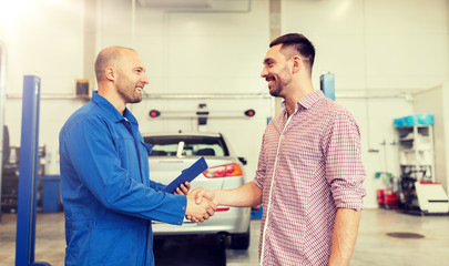 Obraz premium auto service, repair, maintenance, gesture and people concept - mechanic with clipboard and man or owner shaking hands at car shop
