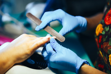 Manicurist master make manicure in blue gloves with nail file. Woman getting nail manicure