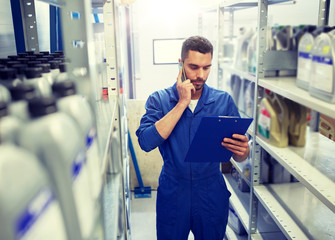 car service, repair, maintenance and people concept - auto mechanic man or smith with clipboard calling on smartphone at workshop or warehouse