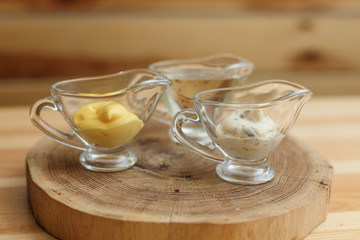 Set of three transparent sauceboats with different sauces on wooden plate