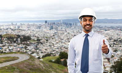 architecture, construction business and building - smiling indian architect or businessman in helmet showing thumbs up over san francisco city background