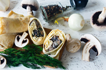 Pancakes with mushrooms on a wooden board on a white background. Russian traditional snack. Mushrooms, onions, herbs, spices