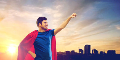 Fototapeta na wymiar super power and people concept - happy young man in red superhero cape over sunset in city of tallinn background